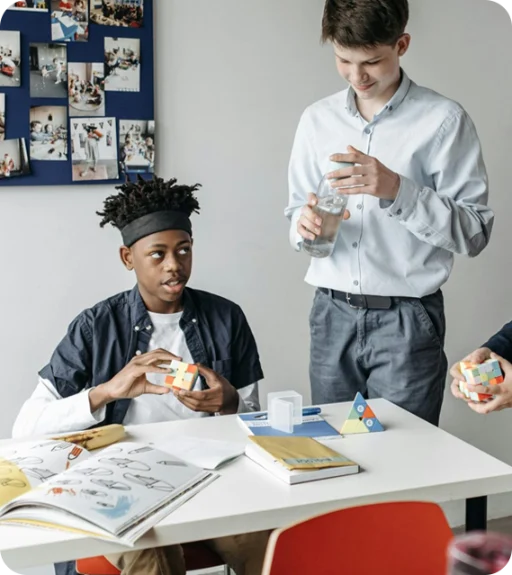 Two kids, one is playing with a rubiks cube, and the other is holding a bottle of water.