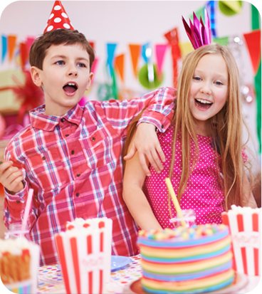 Two kids with hats in front of a cake.